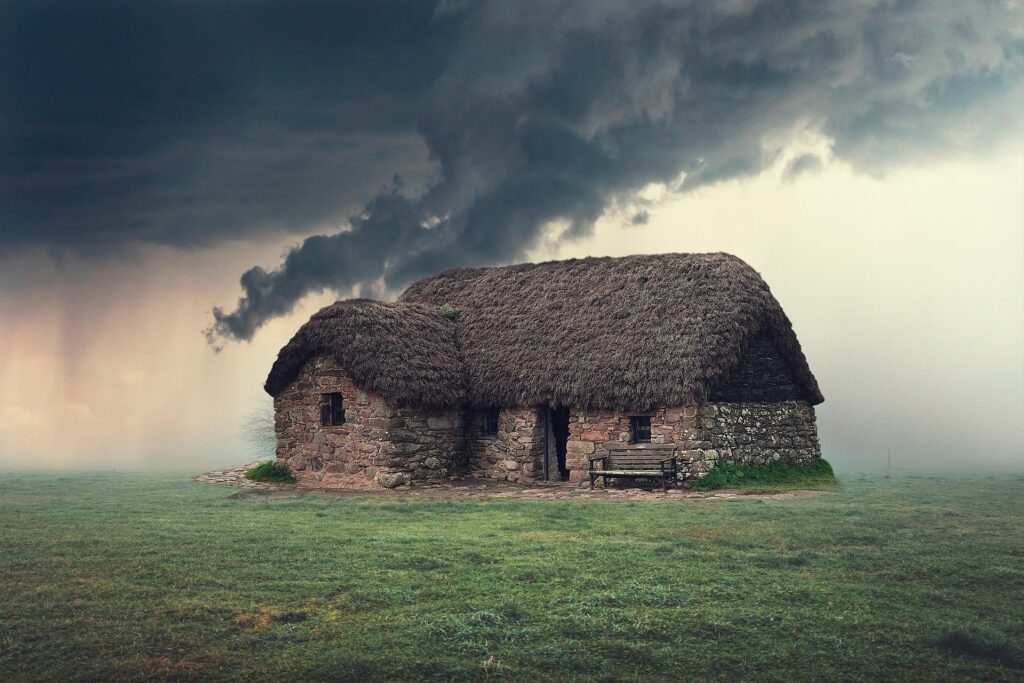 Thatched-roof cottage amidst a dramatic sky, showcasing rustic architecture and a serene, green landscape, evoking a sense of tranquility.