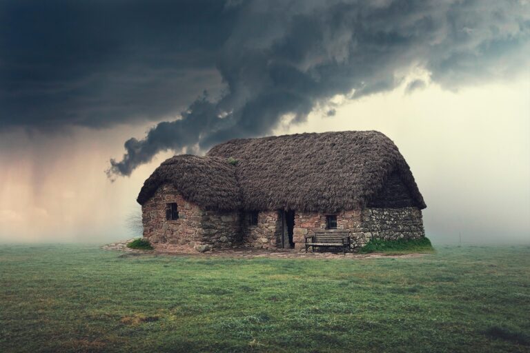 Thatched-roof cottage amidst a dramatic sky, showcasing rustic architecture and a serene, green landscape, evoking a sense of tranquility.