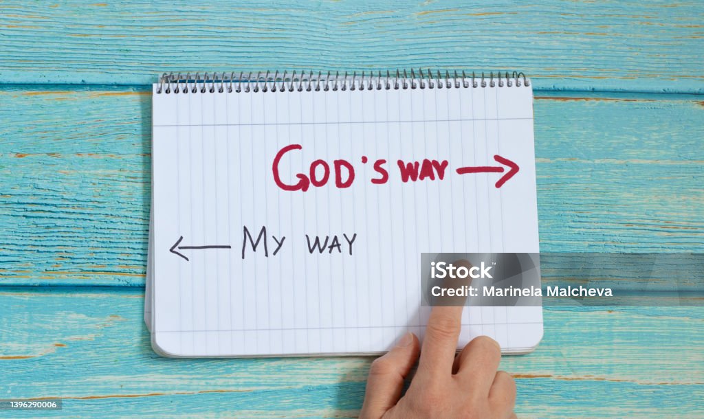 God's way, message quote on a notebook with a hand showing in direction to handwritten arrow isolated on a light blue wooden background. Top view. Follow Jesus Christ's path of eternal life concept.
