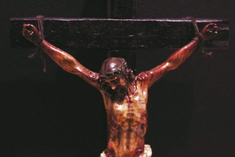 Crucifix depicting Jesus on the cross, showcasing detailed woodwork and dark background, symbolizing Christian faith and sacrifice.