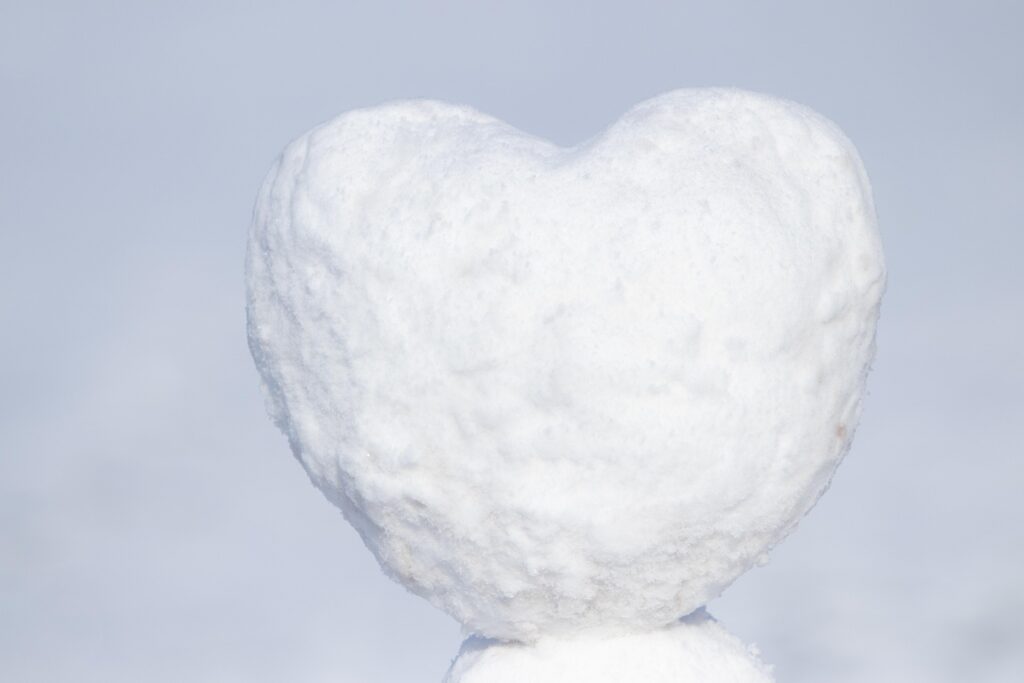 A heart-shaped snow sculpture stands prominently against a pale background, symbolizing winter's beauty and creativity.