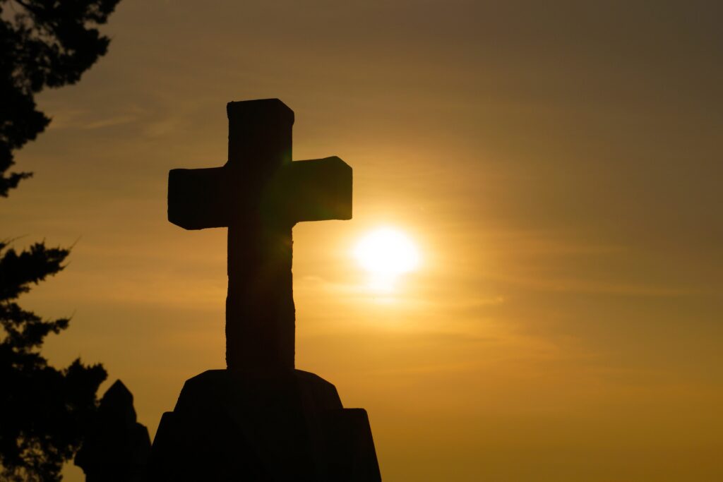 Silhouetted cross against a warm sunset sky, evoking themes of remembrance and spirituality in a serene setting.