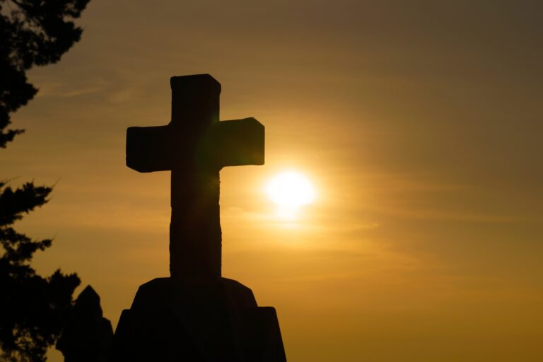 Silhouetted cross against a warm sunset sky, evoking themes of remembrance and spirituality in a serene setting.