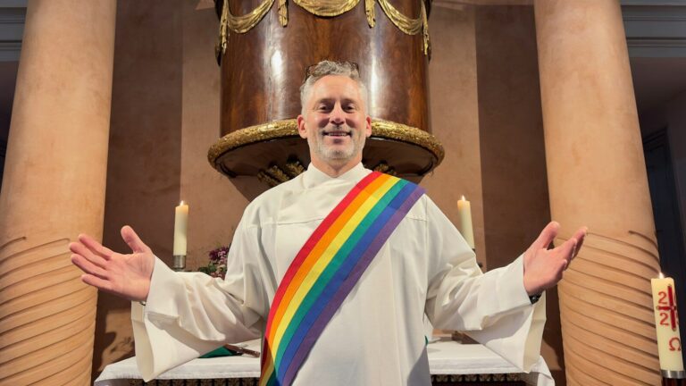 A man in religious vestments with a rainbow stole