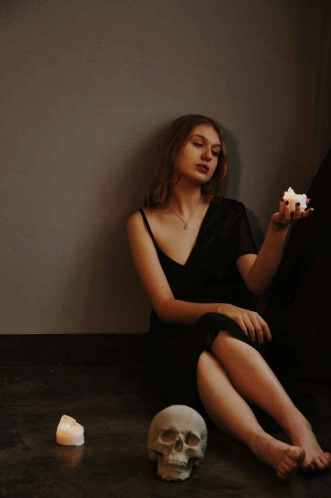 Young woman with candle and skull sits on floor